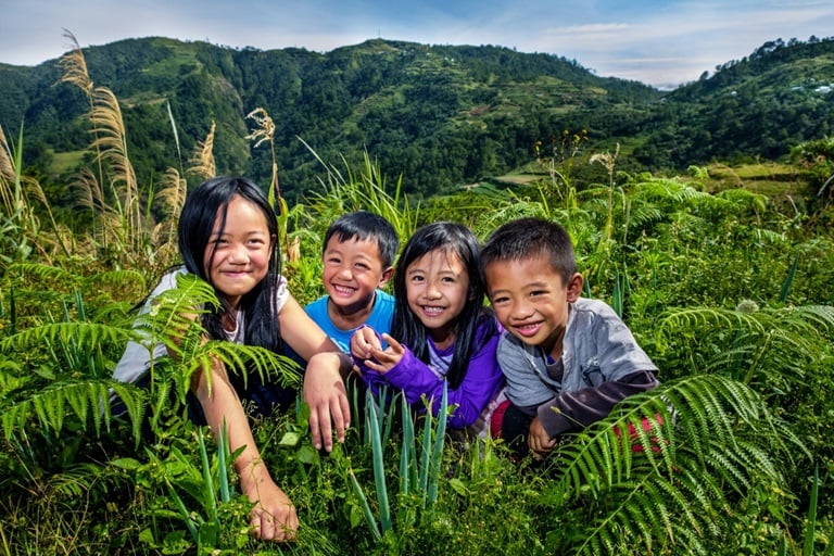 Four children kneel down in a field with big smiles on their faces