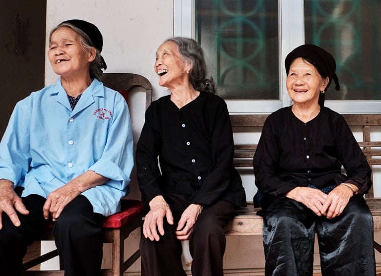 Three older women sit on a bench laughing